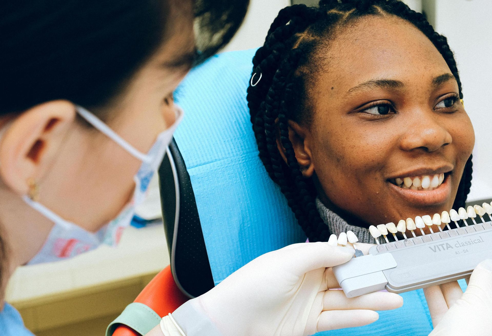 Cheerful black woman sitting in dental chair of modern dentist office and checking teeth implant while looking away