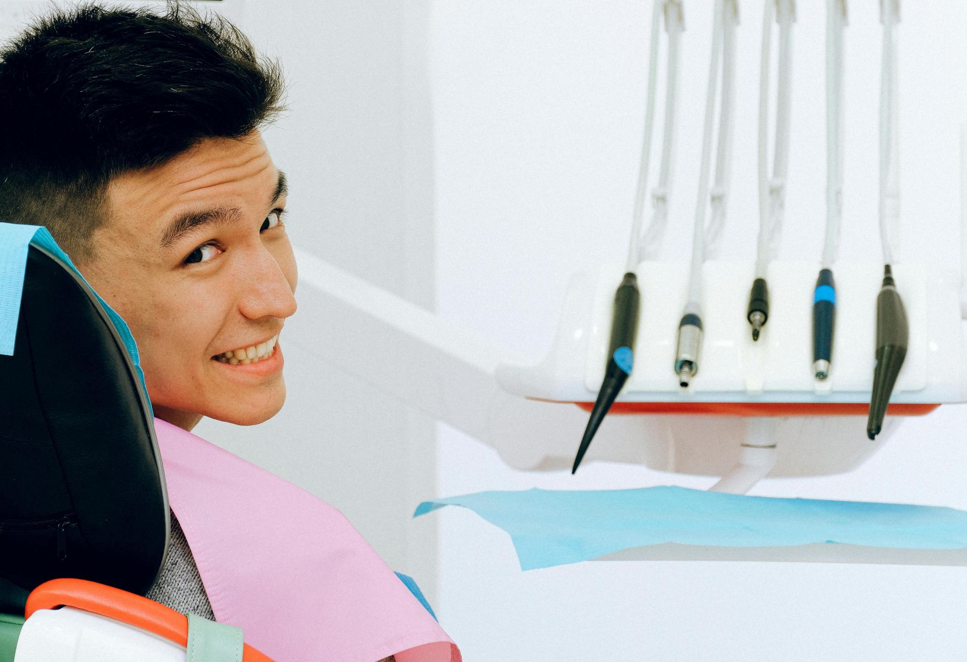 Back view of smiling ethnic man sitting in chair of dentist while preparing for treatment in modern clinic and looking over shoulder at camera